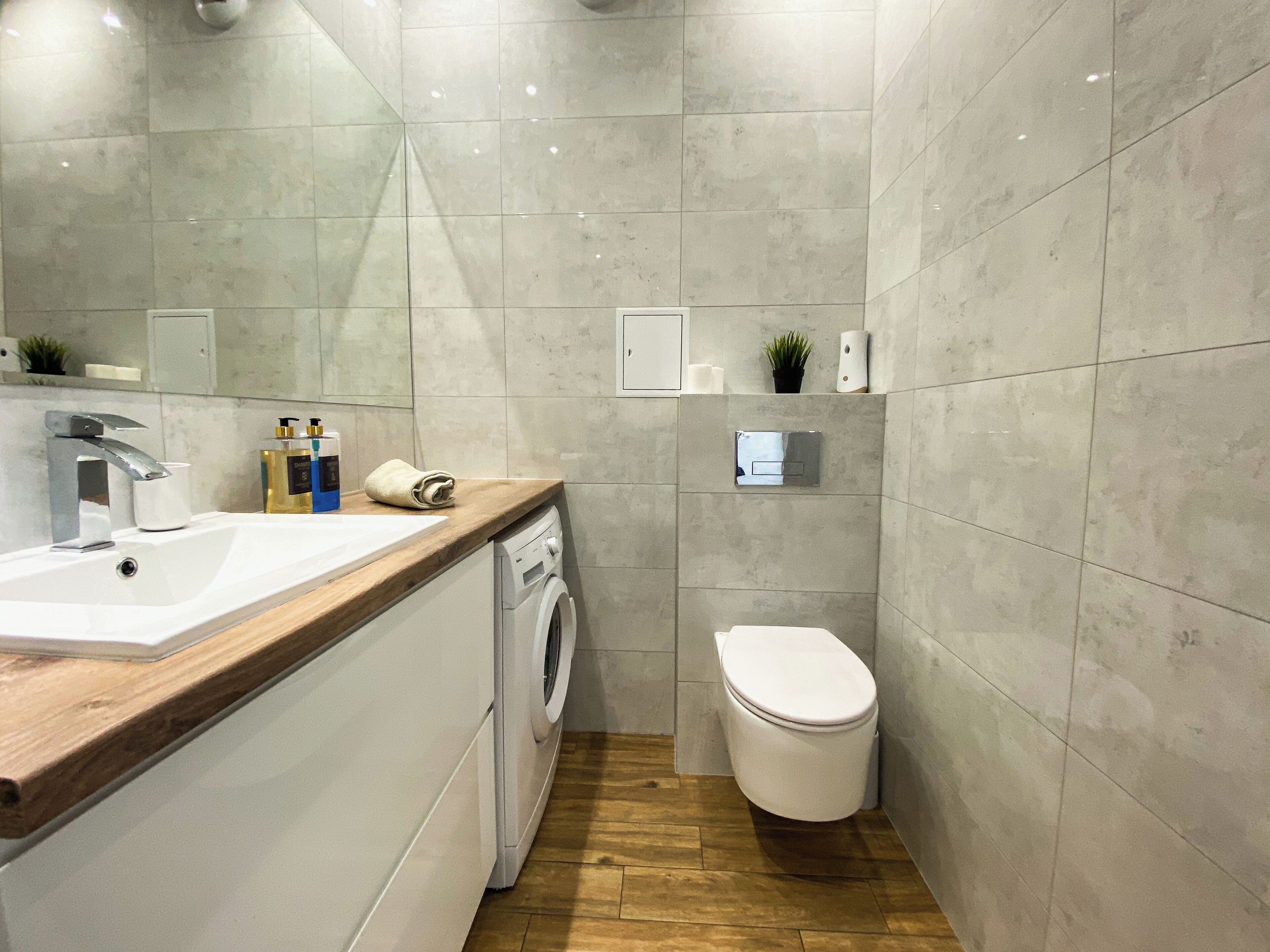 Ein modernes Badezimmer mit Holztischplatte, Waschbecken, Waschmaschine, Toilette und Spiegel.