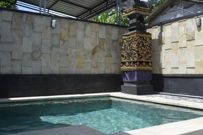 A swimming pool with stone walls and a decorative pillar. - Puri Bintang (Nusa Dua)