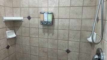 A tiled shower area with a handheld showerhead, a soap dispenser, and a soap dish.