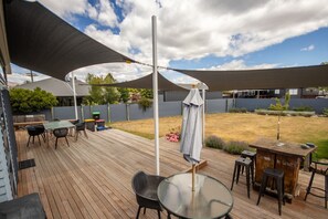 A covered outdoor patio with a wooden deck, a round glass table, and a bar area. - Tussock Retreat - Modern Open Plan, Huge Deck (Twizel)