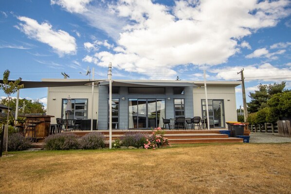 A modern two-story house with a covered patio, large windows, and a well-maintained lawn. - Tussock Retreat - Modern Open Plan, Huge Deck (Twizel)