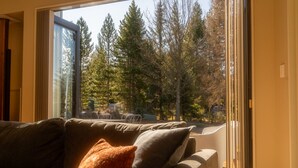 Ein Wohnzimmer mit großem Fenster, einer Couch und Blick auf Bäume und einen Zaun.