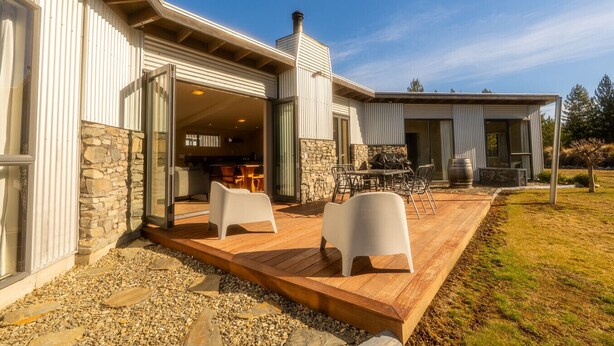 Ein modernes Haus mit Natursteinfassade, einer Holzterrasse und einer Patio mit Gartenmöbeln.