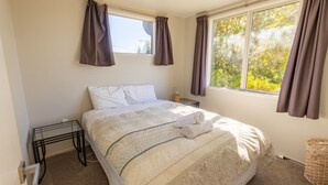 Ein Schlafzimmer mit Bett, Nachttisch, Fenster mit Vorhängen und Blick ins Grüne.