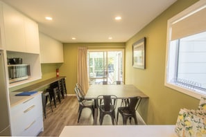 A compact kitchen with a dining area, white cabinets, a microwave, and a window with blinds.