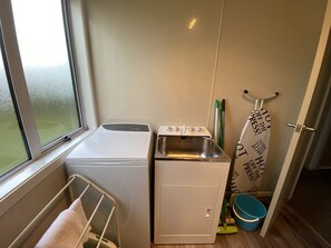 A compact laundry area with a washing machine, a small sink, and a drying rack.