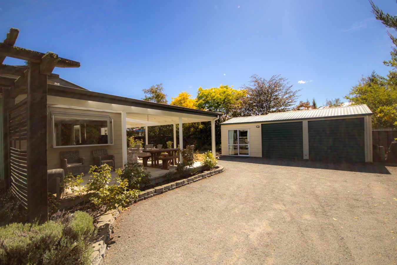 Eine überdachte Terrasse mit Gartenmöbeln, eine Garage und ein gepflegter Schotterweg.