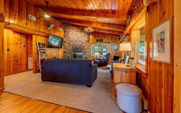 A log cabin interior with a stone fireplace, a black sofa, a television, and a stone wall.