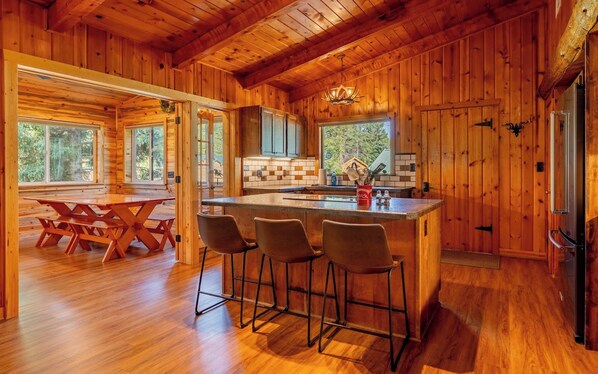 Interior de una cabaña de madera con cocina, barra y comedor.