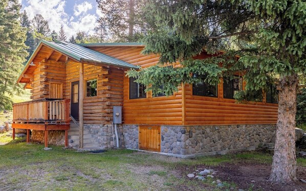 A log cabin with a stone foundation, wooden deck, and large windows.