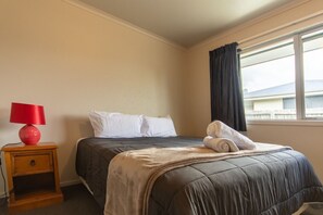 Ein Hotelzimmer mit einem Bett, einem Nachttisch mit Lampe und einem Fenster mit Vorhängen.