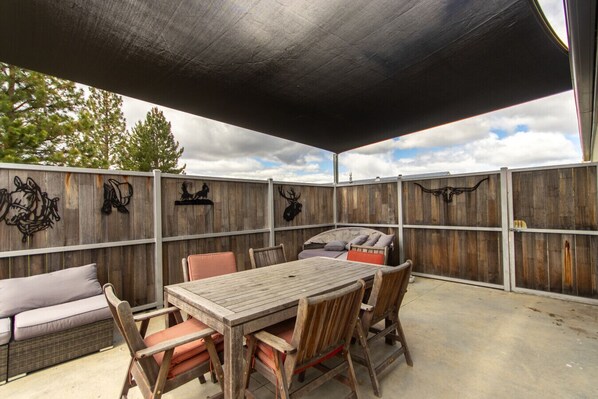 Eine Terrasse im Freien mit einem Holztisch und -stühlen, einem Grill und dekorativer Wandgestaltung.