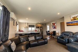 Ein modernes Wohnzimmer mit einer Ledersofa, einem Essbereich mit Holztisch und Stühlen sowie einer Küche mit Edelstahlgeräten.