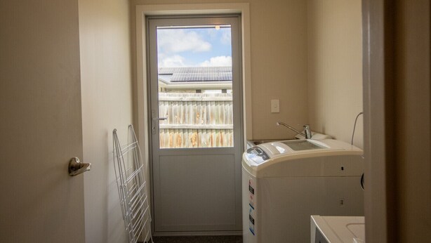 Un lavadero con lavadora, secadora y una puerta que da a un balcón con vista a un edificio.