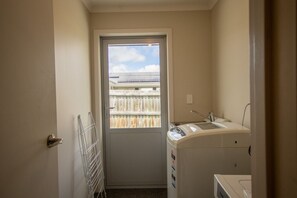 Une buanderie équipée d’un lave-linge, d’un sèche-linge et d’une porte donnant sur un balcon avec vue sur un immeuble.