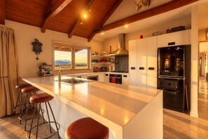 A modern kitchen with a large island, bar stools, and a view of mountains through the window.