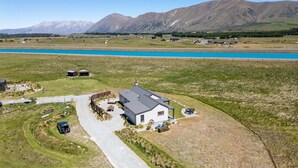 A modern house with a paved driveway, a fenced yard, and a mountain backdrop.