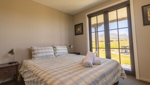 A bedroom with a large bed, a nightstand, a lamp, and a window with a view of a landscape.