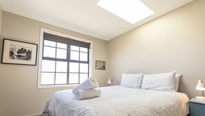 A bedroom with a large window, a bed with white linens, two bedside lamps, and a framed picture on the wall.