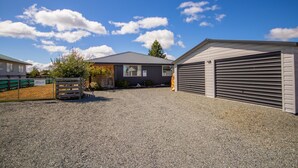 A building with a gravel driveway, a wooden gate, and a covered garage. - New with a View, Twizel - FREE WIFI (Twizel)