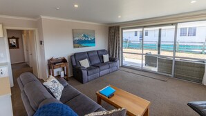 A living room with a grey sofa, a blue ottoman, and a wooden coffee table. There is a painting on the wall and a sliding glass door leading to an outdoor area. - New with a View, Twizel - FREE WIFI (Twizel)