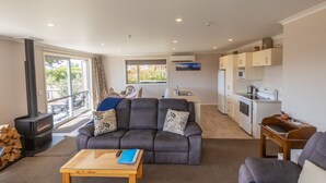 A modern living room with a grey sofa, a wooden coffee table, and a kitchen area with white cabinets and appliances. - New with a View, Twizel - FREE WIFI (Twizel)