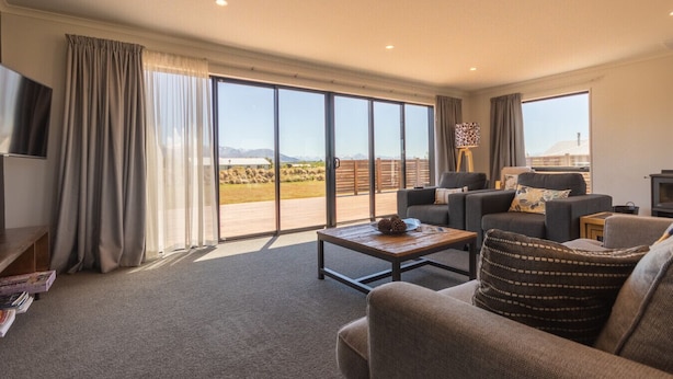 A spacious living room with a large sliding glass door leading to an outdoor area, a flat-screen TV mounted on the wall, and a fireplace.
