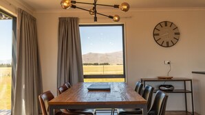 A dining room with a wooden table, chairs, a chandelier, a clock, and a view of mountains.