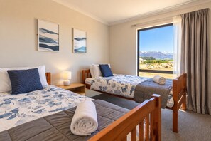 A hotel room with two beds, a large window with a mountain view, and artwork on the wall.