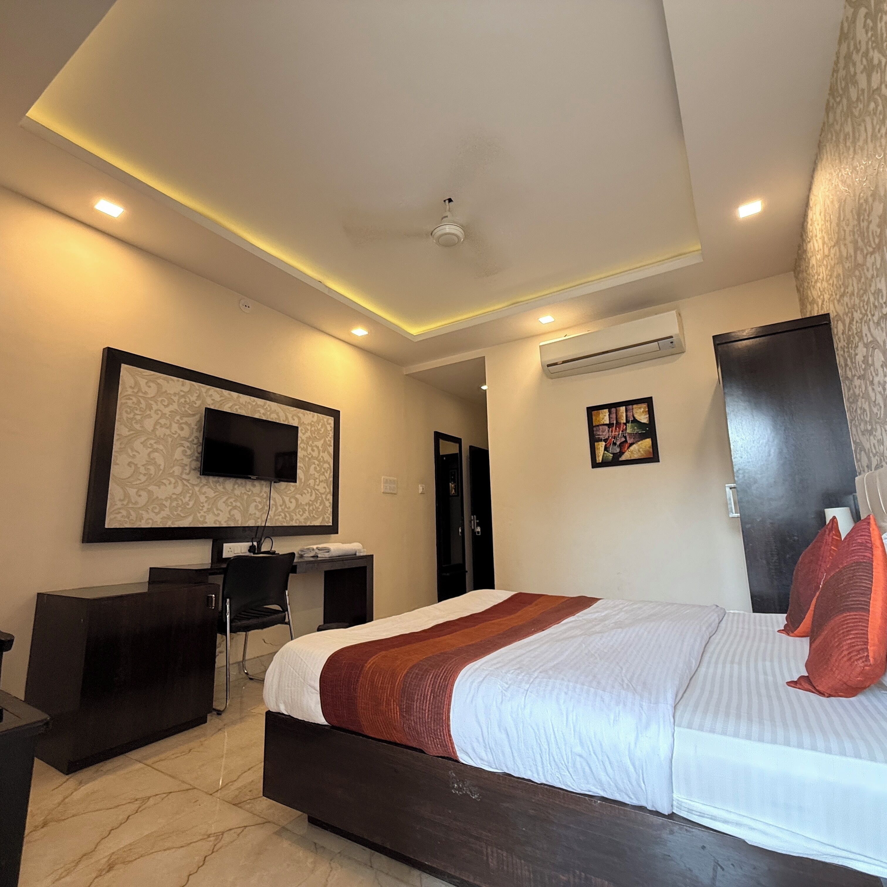 A modern hotel room with a large bed, a desk, a flat-screen TV, and an air conditioning unit.