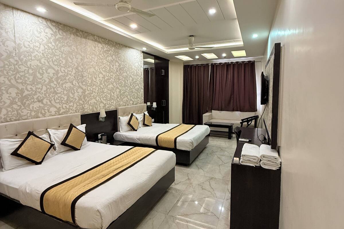 A hotel room with two beds, a desk, a chair, a TV, and a ceiling fan.