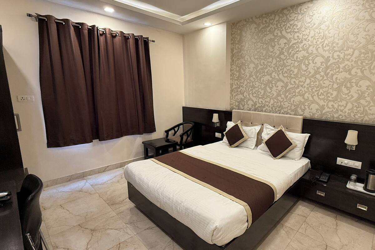 A hotel room with a large bed, a bedside table, a chair, and a desk.