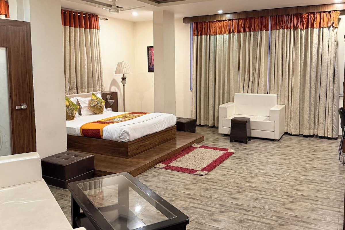 A modern hotel room with a wooden bed, a glass coffee table, a white sofa, and a large window with curtains.