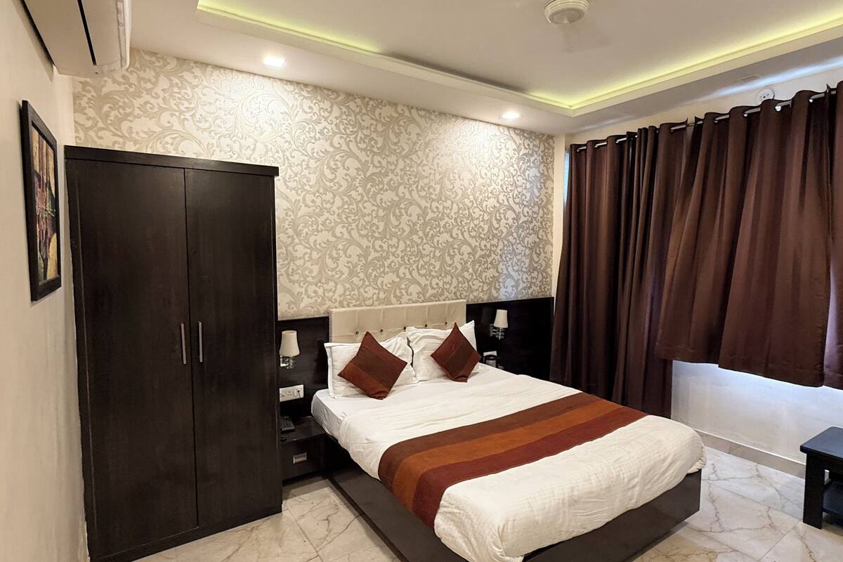 A bedroom with a large bed, dark wardrobe, patterned wallpaper, and a ceiling fan.