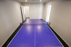 A room with a ping pong table, a door, and a small red object on the table.