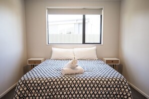 A neatly made bed with a patterned bedspread, two bedside tables, and a window with blinds. - Mackenzie Magic, Twizel - FREE WIFI (Twizel)