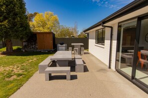 An outdoor patio with a concrete table and benches, a wooden shed, and a fenced yard.
