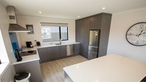 Una cocina moderna con armarios grises, un refrigerador de acero inoxidable, una cafetera y un reloj de pared grande.