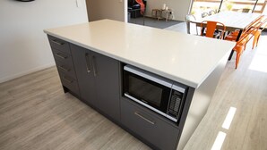 Una cocina moderna con microondas integrado, armarios grises y encimera de color claro.
