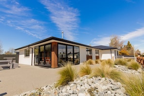A modern house with a large glass front, a wooden deck, and a stone pathway.