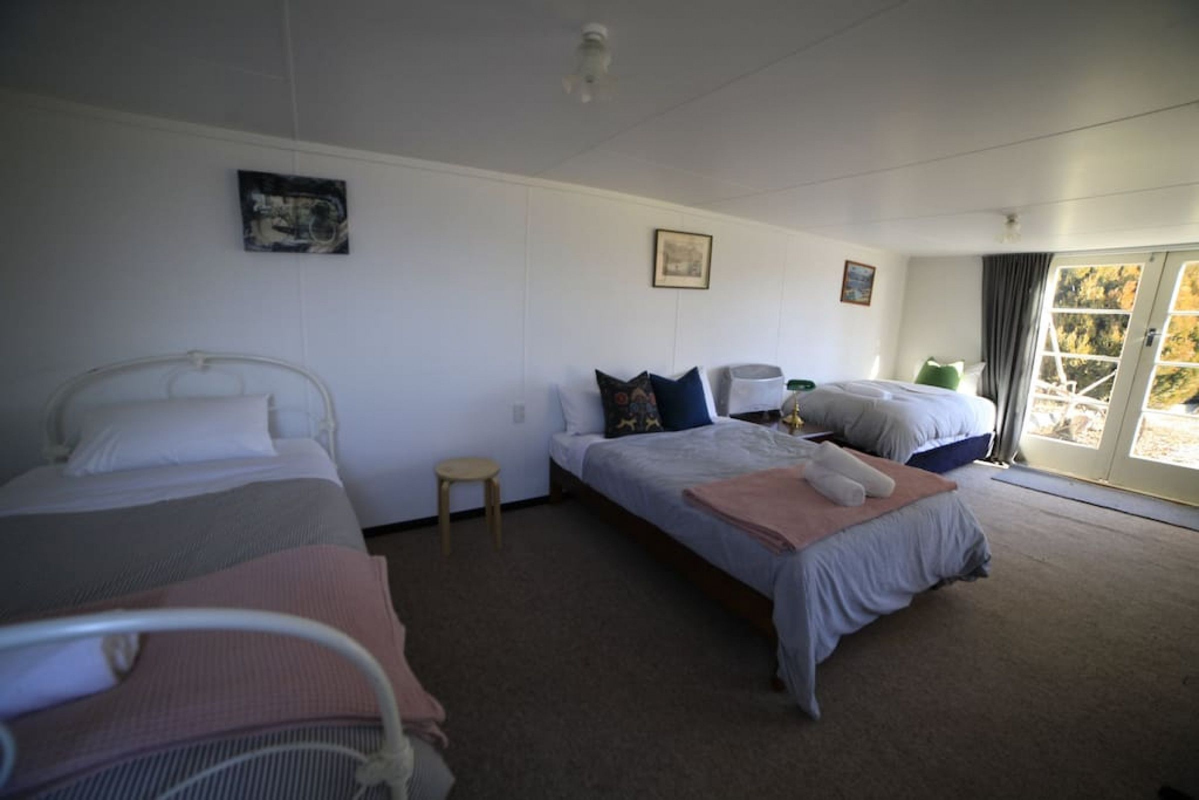 A hotel room with two beds, a small stool, and a sliding glass door to the outside.