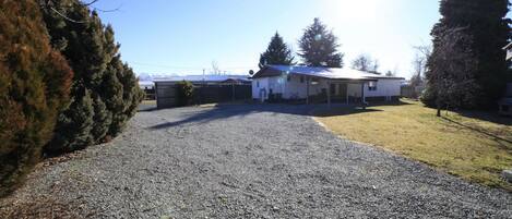 A gravel driveway leading to a white building with a covered porch, surrounded by trees and a clear sky.