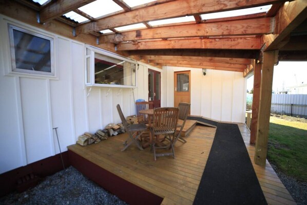 A covered patio area with a wooden deck, a table with chairs, and a door leading to a white room.