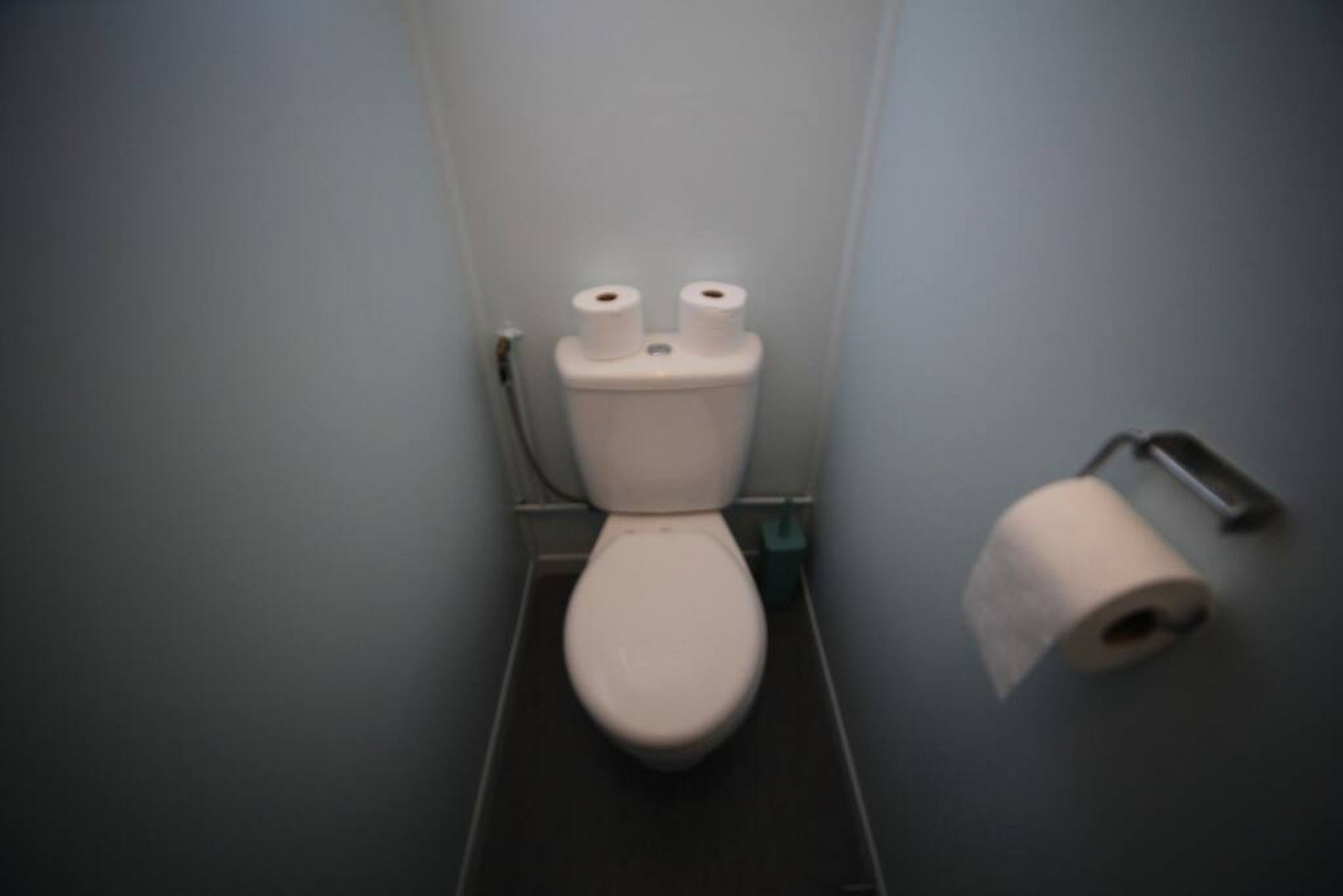 Ein kleines, schmales Badezimmer mit Toilette, zwei Toilettenpapierrollen und einem Papierhandtuchspender.