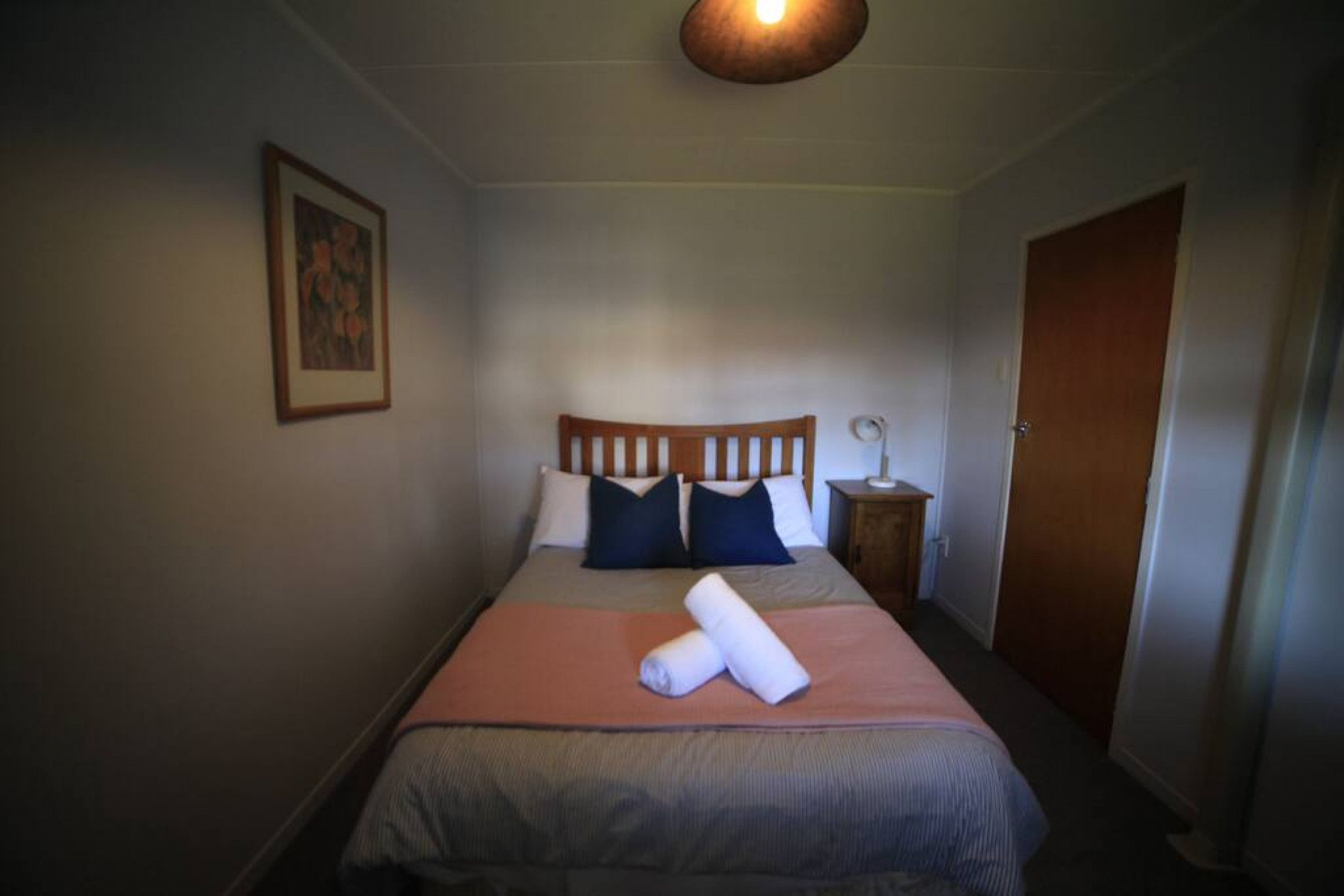 A bedroom with a bed, pillows, a bedside table, a lamp, and a door.