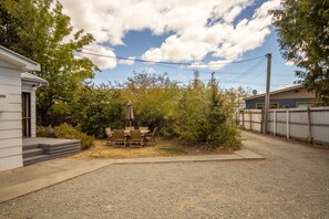 A residential area with a gravel driveway, a wooden table and chairs, and a small patio area.