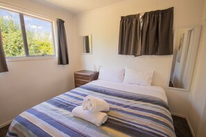A hotel room with a bed, a nightstand, a window, and curtains.