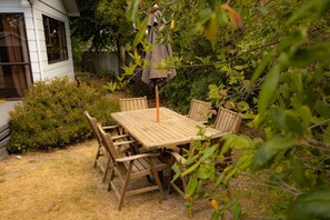 A wooden patio table with four chairs, surrounded by dense foliage and a wooden fence.