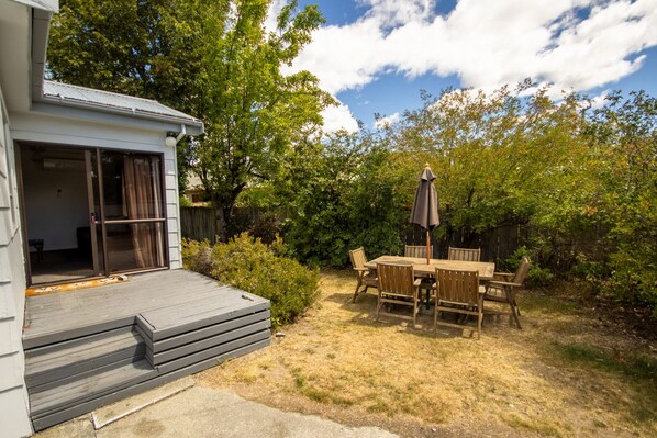 A patio with a table and chairs, surrounded by a wooden deck and a covered umbrella.