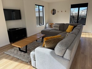 A modern living room with a grey sofa, a wooden bench, and a flat-screen TV mounted on the wall.
